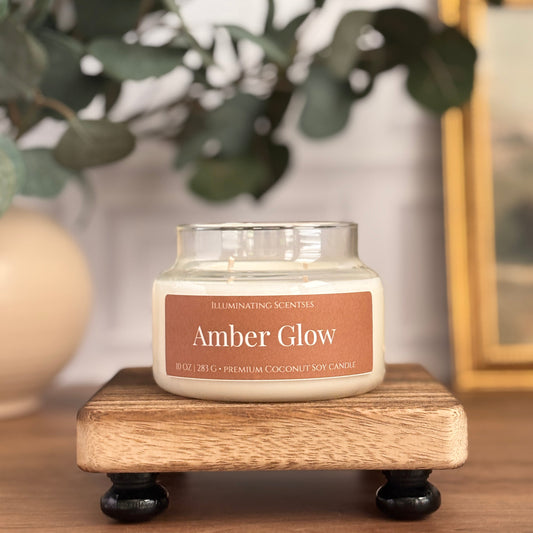 Amber Glow jar candle by Illuminating Scentses with the lid removed, displayed on a wooden stand.