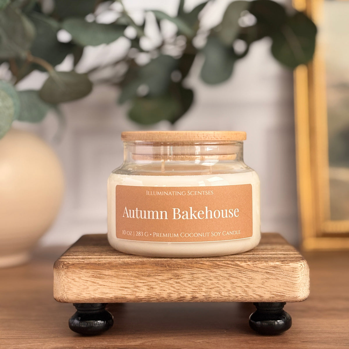 Autumn Bakehouse jar candle by Illuminating Scentses with the lid on, displayed on a wooden stand.
