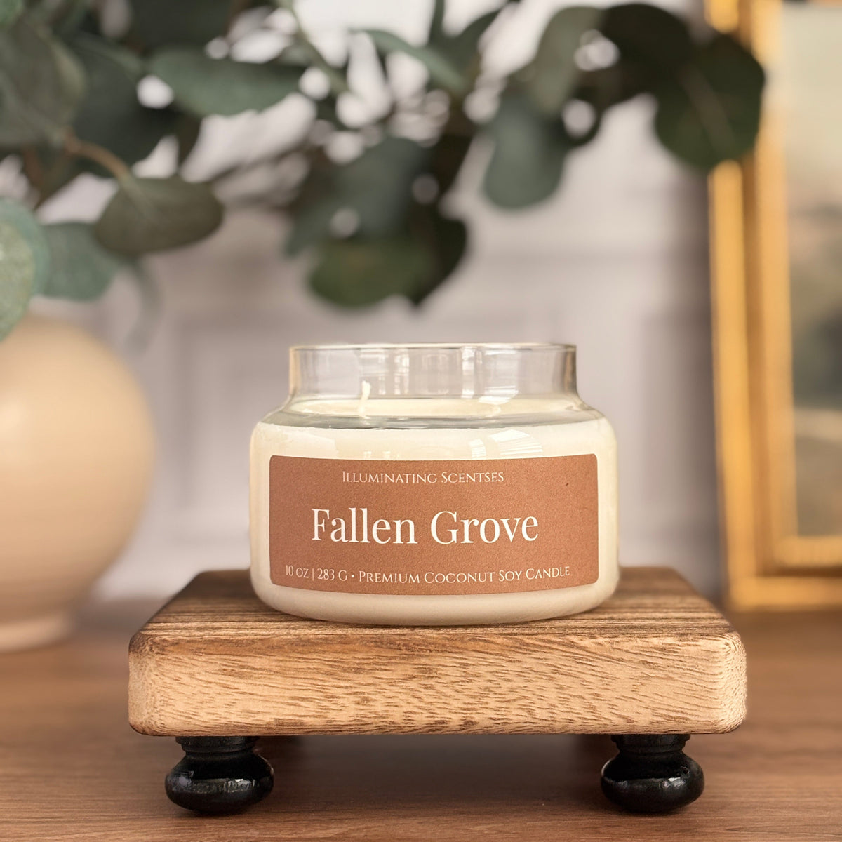 Fallen Grove jar candle by Illuminating Scentses with the lid removed, displayed on a wooden stand.