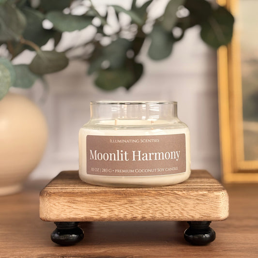 Moonlit Harmony jar candle by Illuminating Scentses on a wooden stand, with blurred greenery and a vase in the background